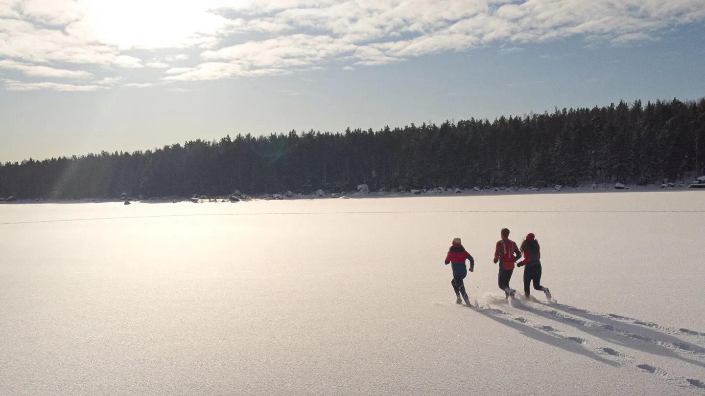 Tre personer som går på en snötäckt is över skärgården
